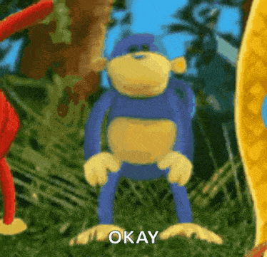 a blue and yellow stuffed monkey is standing in the grass and saying okay
