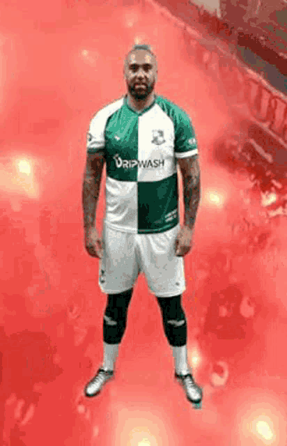 a man in a green and white dripwash jersey stands on a red background