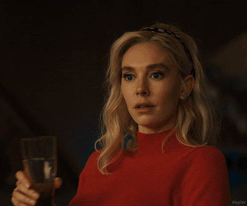 a woman in a red sweater holds a glass of water in her right hand