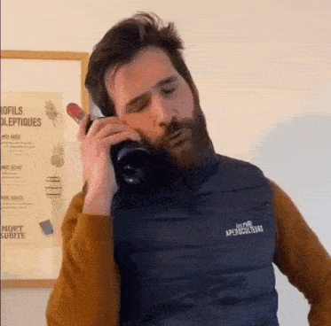 a man with a beard is holding a bottle of wine and talking on a cell phone .