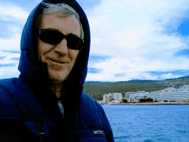 a man wearing sunglasses and a hooded jacket has a sticker on his jacket that says ' national geographic ' on it