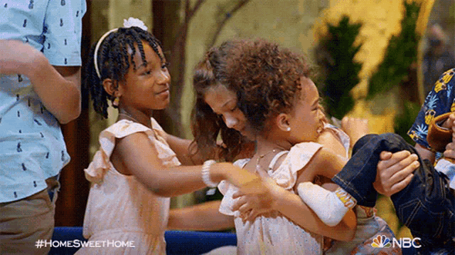two little girls are hugging each other while a man holds a baby .