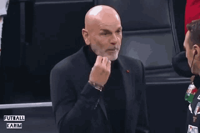 a man in a suit and turtleneck is sitting in a stadium with a bottle of coca cola in his hand .