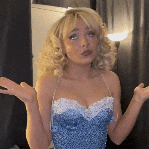 a blonde woman wearing a blue and white dress making a funny face