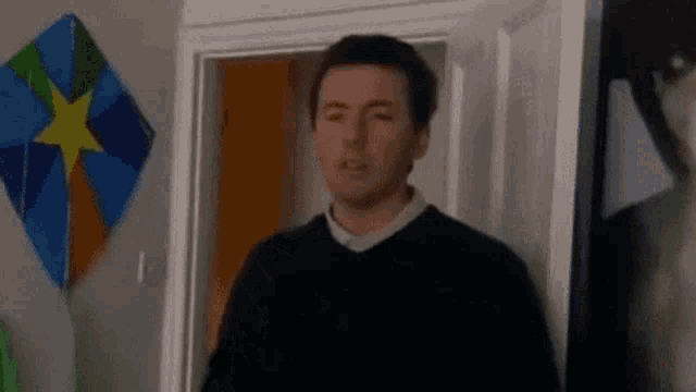 a man is standing in a doorway with a kite hanging on the wall behind him .