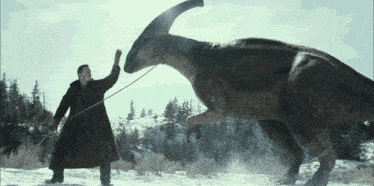a man in a trench coat stands next to a large dinosaur in the snow