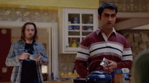 a man in a red and white striped shirt is standing in a kitchen holding a blue teapot