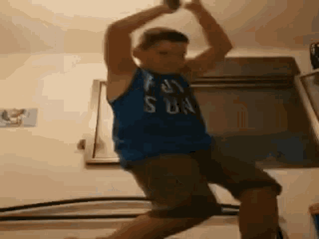 a young boy in a blue tank top is jumping in the air while holding a can .