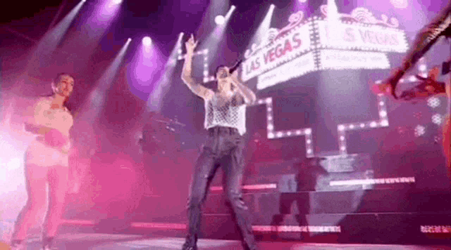a man is singing into a microphone on a stage with a sign that says las vegas in the background .