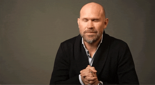 a bald man with his eyes closed and his hands folded