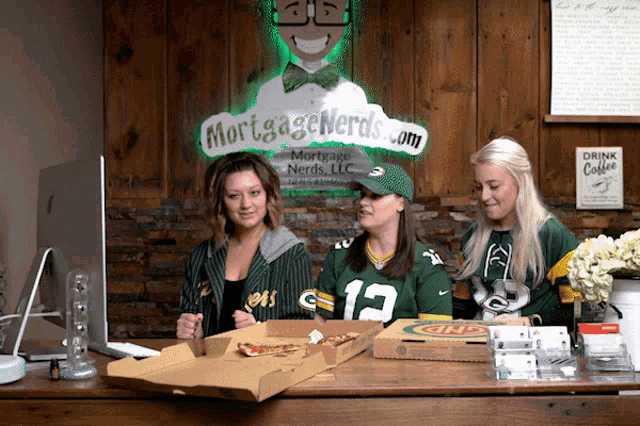 three women sit at a desk in front of a sign for mortgage nerds llc