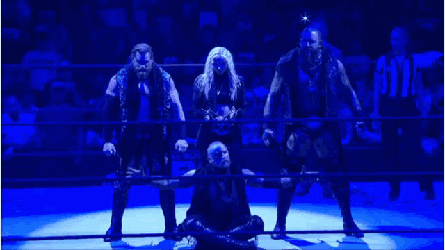a group of wrestlers standing in a ring with a referee in the background