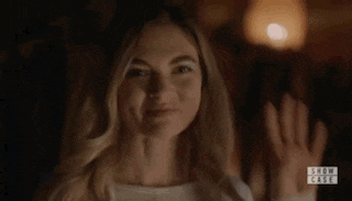 a woman is making a funny face while holding her hand up in the air in a dark room .
