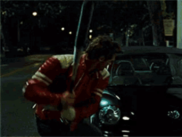 a person in a red jacket is standing next to a car
