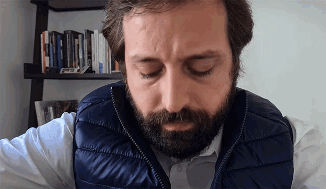 a man with a beard wearing a blue vest looks down