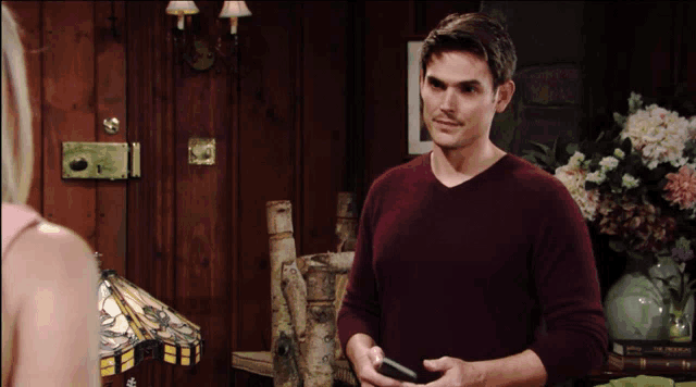 a man in a burgundy sweater is holding a cell phone