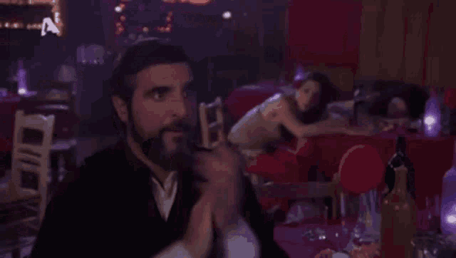 a man with a beard is sitting at a table in a restaurant clapping .