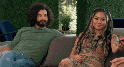 a man and a woman are sitting on a couch and the man has a beard