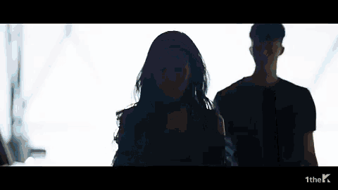 a man and a woman are standing next to each other . the woman is wearing a choker around her neck .