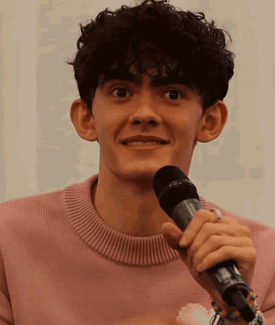 a young man with curly hair is holding a microphone and smiling