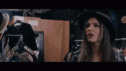 a woman wearing a hat and a leather jacket is standing in front of a rack of clothes .