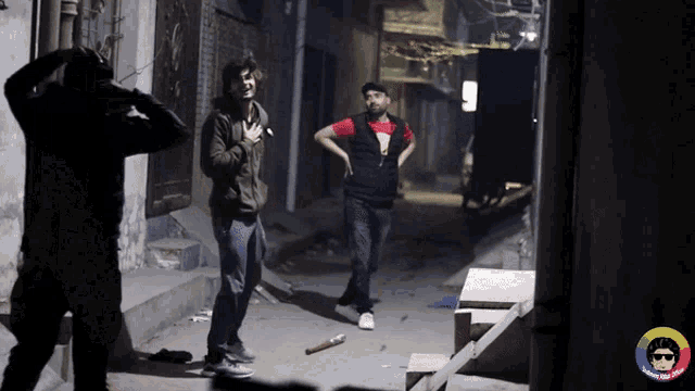a man in a red shirt is standing in a dark alleyway next to a man in a black hoodie