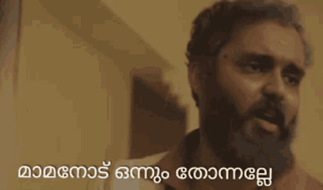 a man with a beard is talking in a room with a caption in malayalam