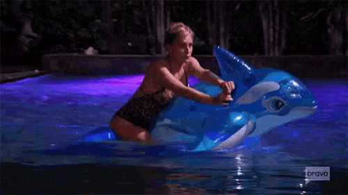 a woman in a swimsuit is riding an inflatable dolphin in a pool .