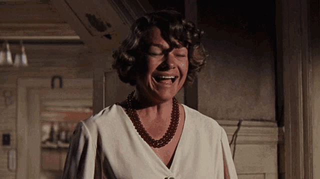 a woman wearing a pearl necklace and a white shirt is laughing