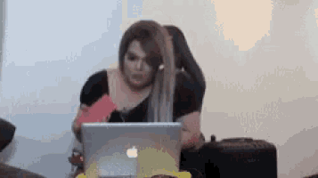 a woman is sitting at a table using an apple laptop .