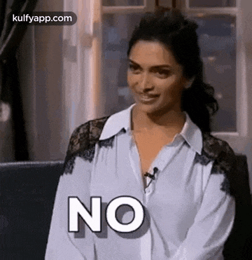 a woman in a white shirt is sitting on a couch and smiling while saying no .