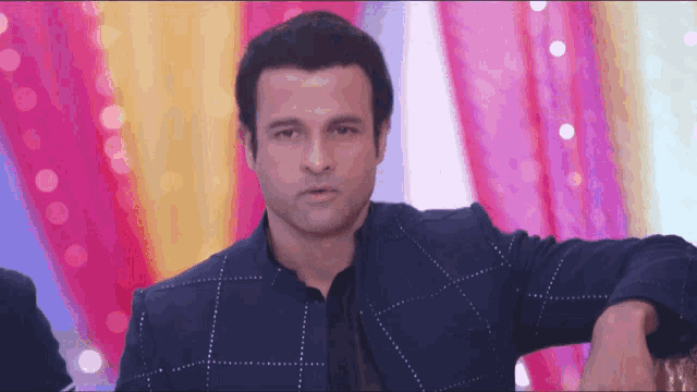 a man in a blue jacket is standing in front of a pink and yellow curtain