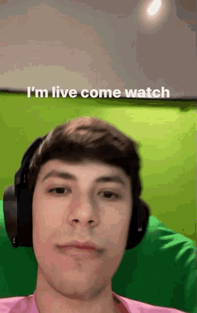 a man wearing headphones says " i 'm live come watch " in front of a green background