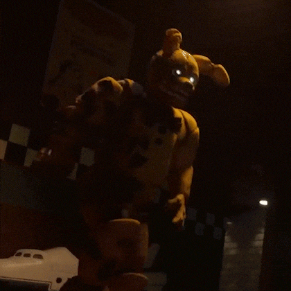 a stuffed animal with glowing eyes is standing in a dark room holding a remote control .