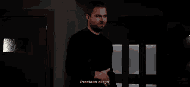 a man in a black shirt is standing in a dark room pointing at a door .