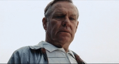 a man in a white shirt and tie is looking at the camera with a serious look on his face .