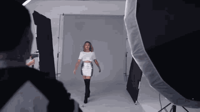 a woman in a white dress and black boots is walking in a photo studio