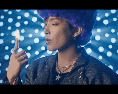 a man with purple hair and a purple hat is holding a lit match .