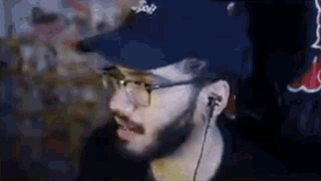 a man with a beard and glasses is wearing a blue hat and earbuds .