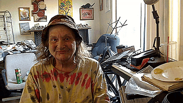 a woman wearing a tie dye shirt and a hat is sitting in front of a piano