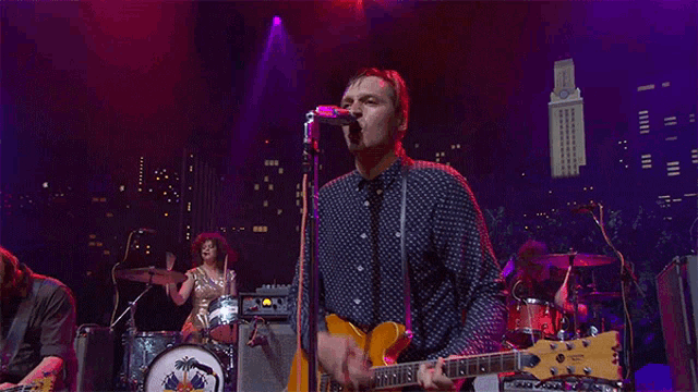 a man singing into a microphone while a woman plays drums in the background
