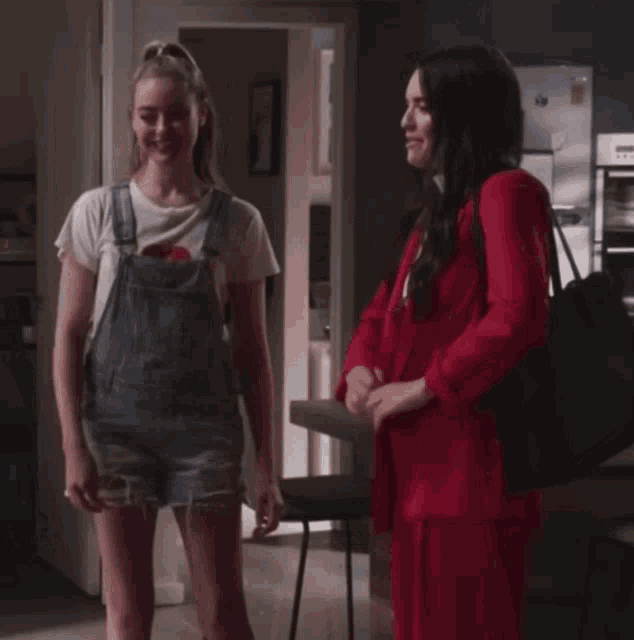 a woman in overalls stands next to another woman in a red suit