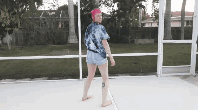 a woman wearing a tie dye shirt and shorts is standing in front of a screened in area