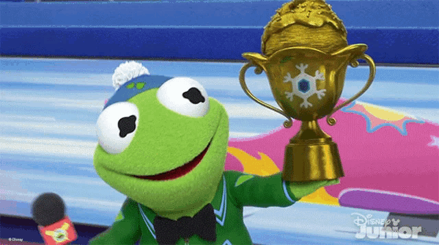 kermit the frog is holding a trophy in front of a disney junior sign
