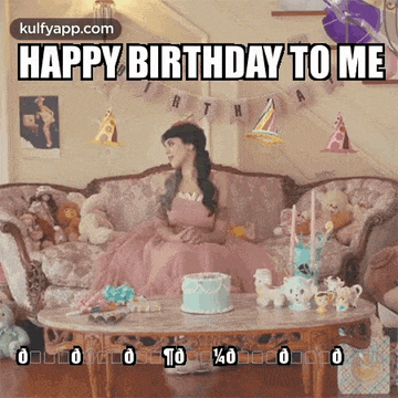 a woman in a pink dress is sitting on a couch next to a table with a birthday cake .