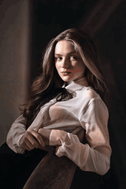 a woman in a white shirt with sheer sleeves is looking at the camera