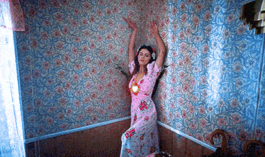 a woman in a pink floral dress is standing in a room with flowers on the walls .