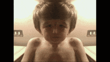 a young boy without a shirt is looking at the camera with his eyes closed
