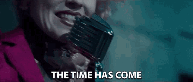 a woman is singing into a microphone with the words `` the time has come '' written below her .