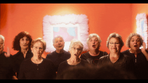 a group of older women singing in front of a red wall